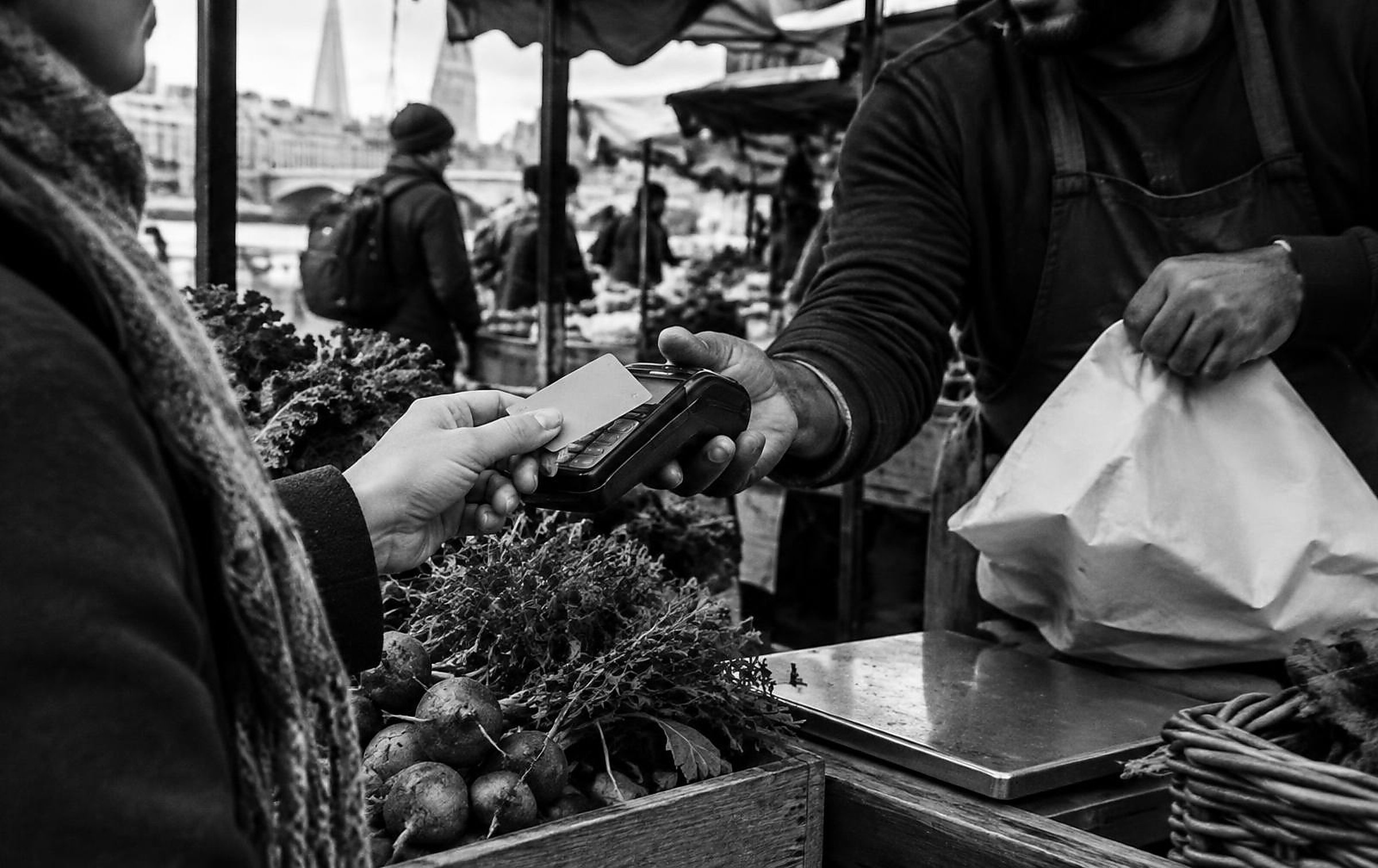 Black and white candid photograph of a contactless card payment at a London market stall