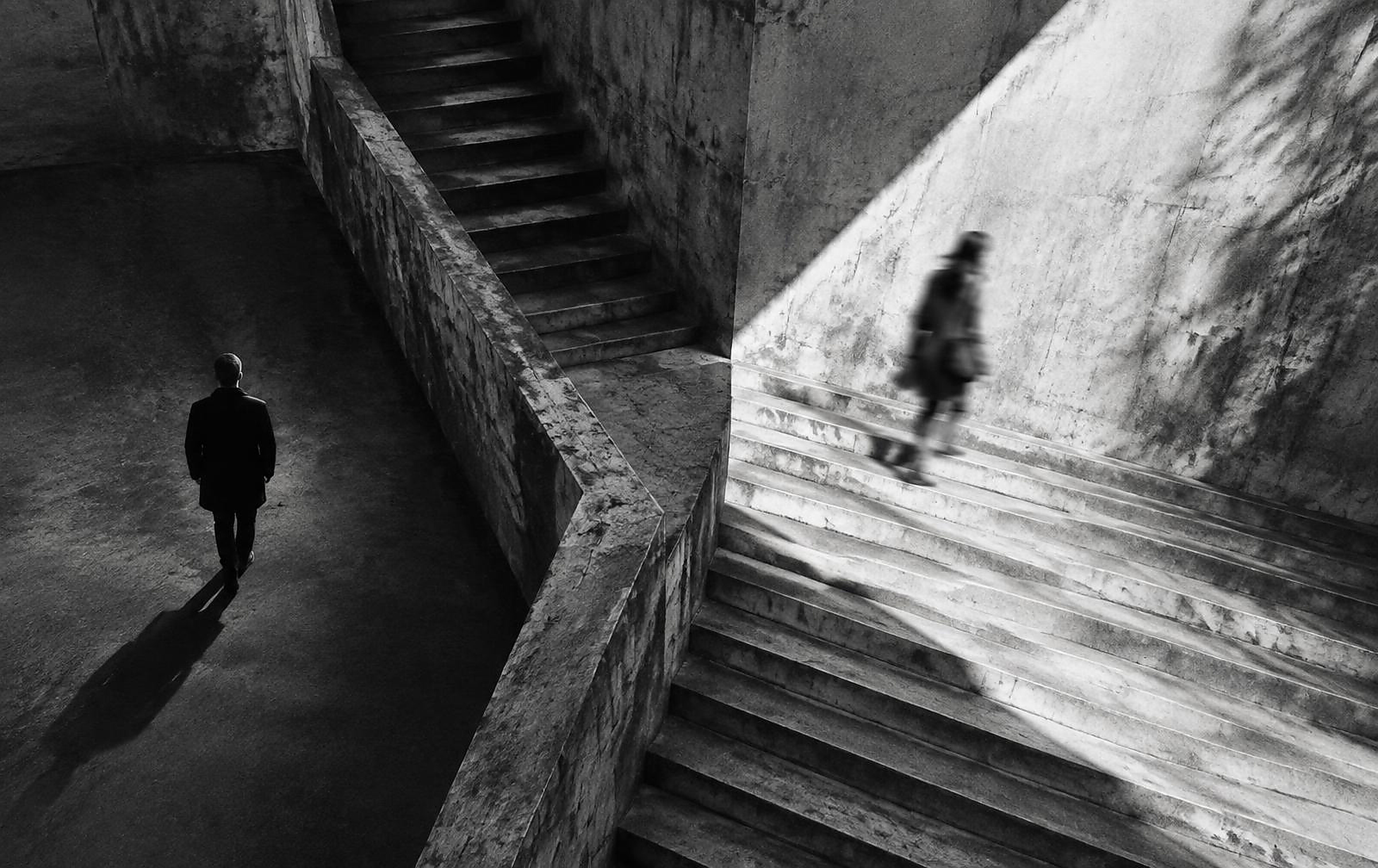 Abstract black and white photograph of two people taking different paths through concrete architecture