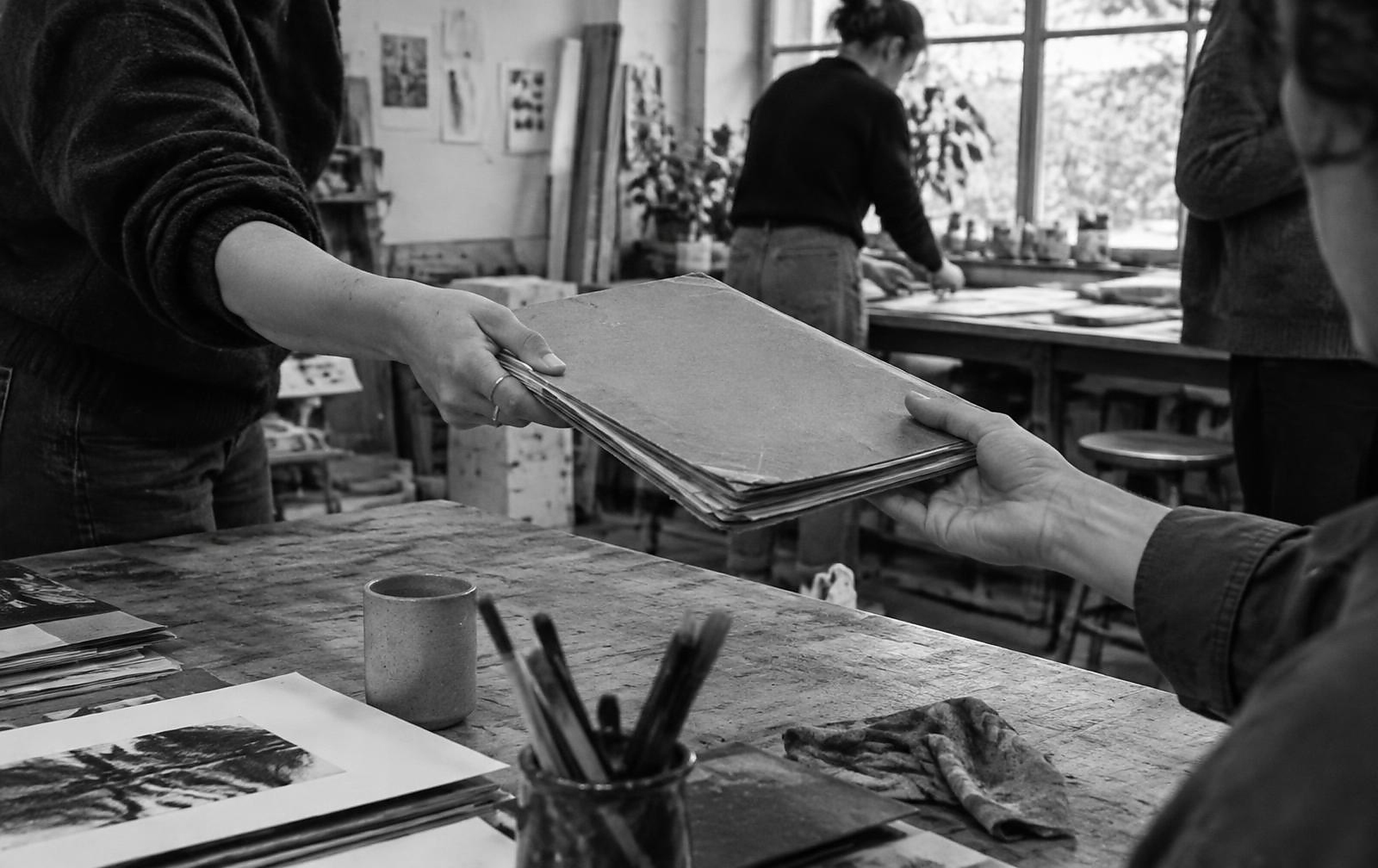 Black and white candid photograph of a worn project folder being handed between colleagues