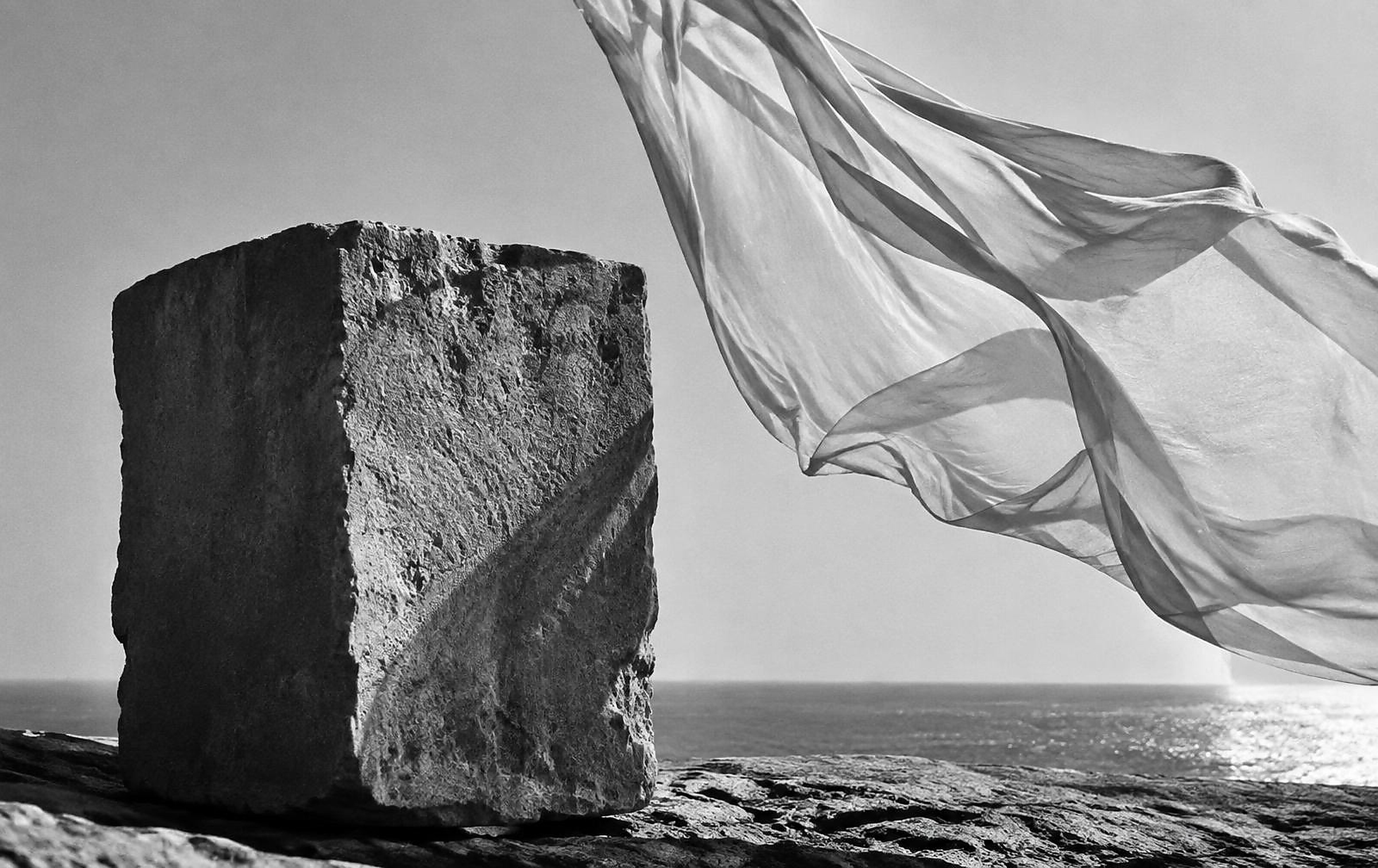 Abstract black and white photograph of solid stone beside fabric moving in the wind