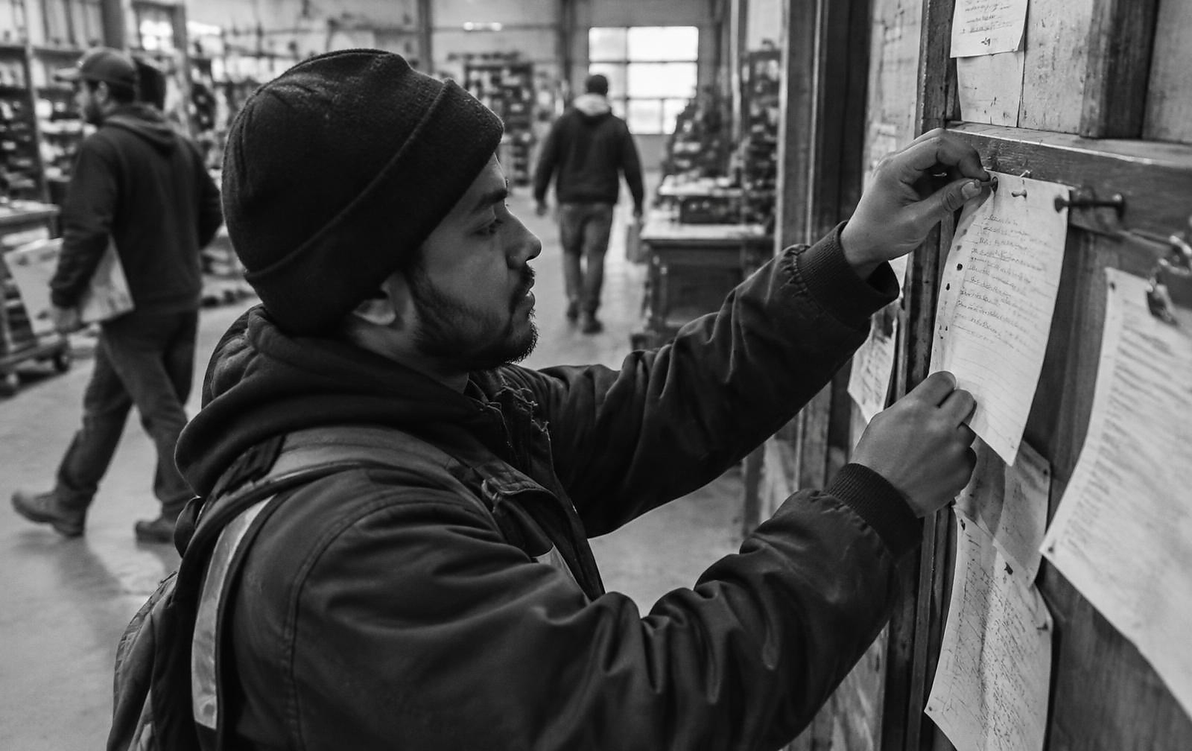 Black and white candid photograph of a workshop note being pinned to a notice rail