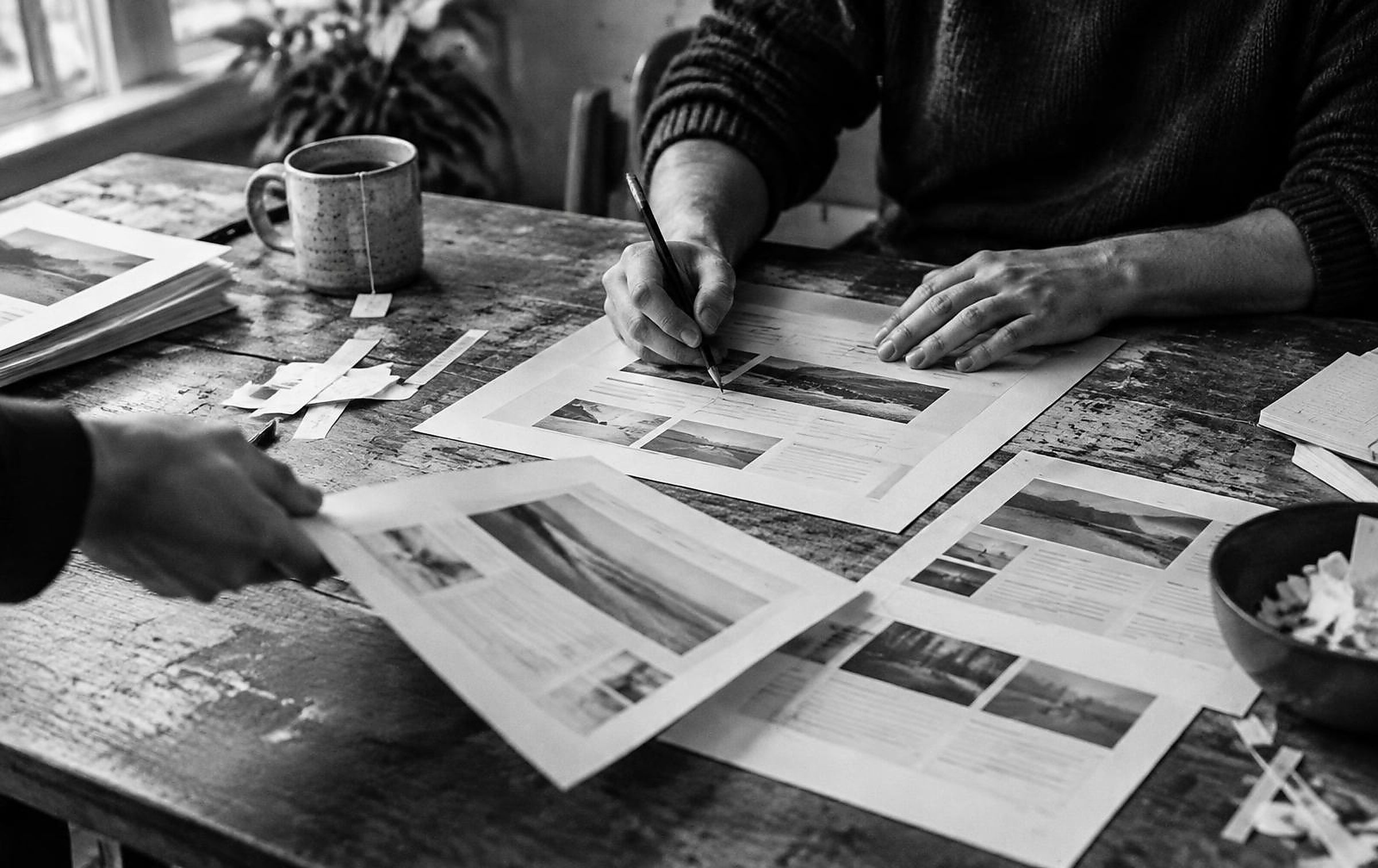 Black and white close photograph of hands marking up printed website layouts